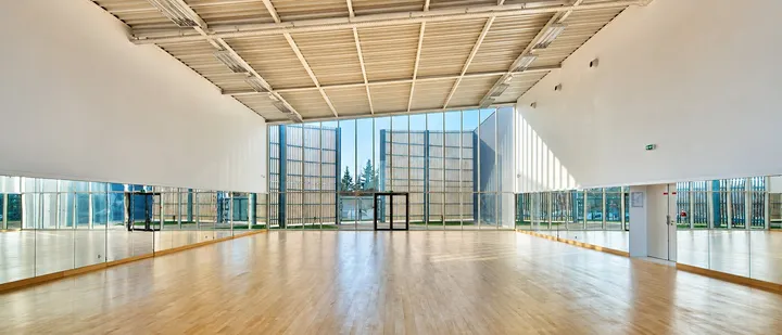 La salle de danse du gymnase Cornuel à Lardy : parquet clair, mur de miroirs et grandes baies vitrées donnant sur les arbres.