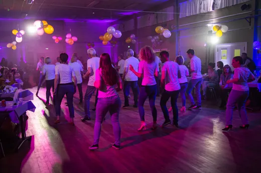 Démonstration de danse en ligne au gala : les danseurs alignés sur la piste sous les lumières violettes, ballons au plafond et public attablé